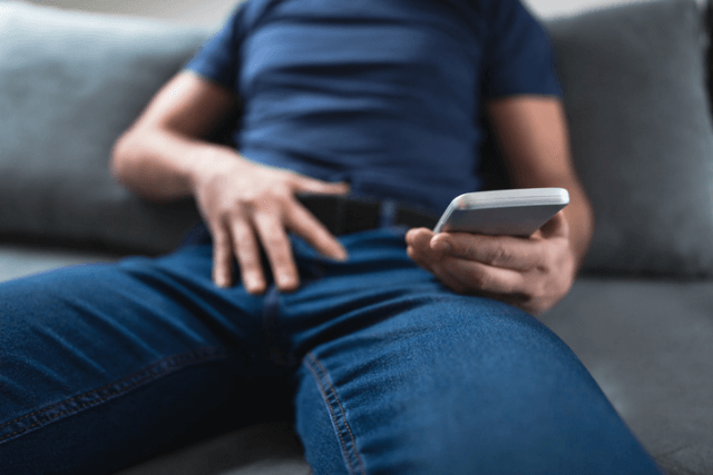iPhoneを見ながらズボンのベルトに手を当てている男性