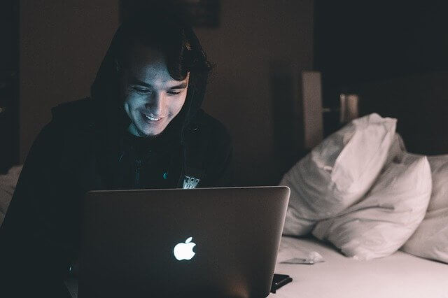 暗い部屋でベッドに座りパソコンを見て笑っている男性
