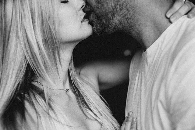 髭が生えている男性の首に手をまわしてキスをする女性