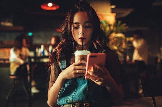 カフェでコーヒーを飲みながらスマホを触るポンパドールの女性